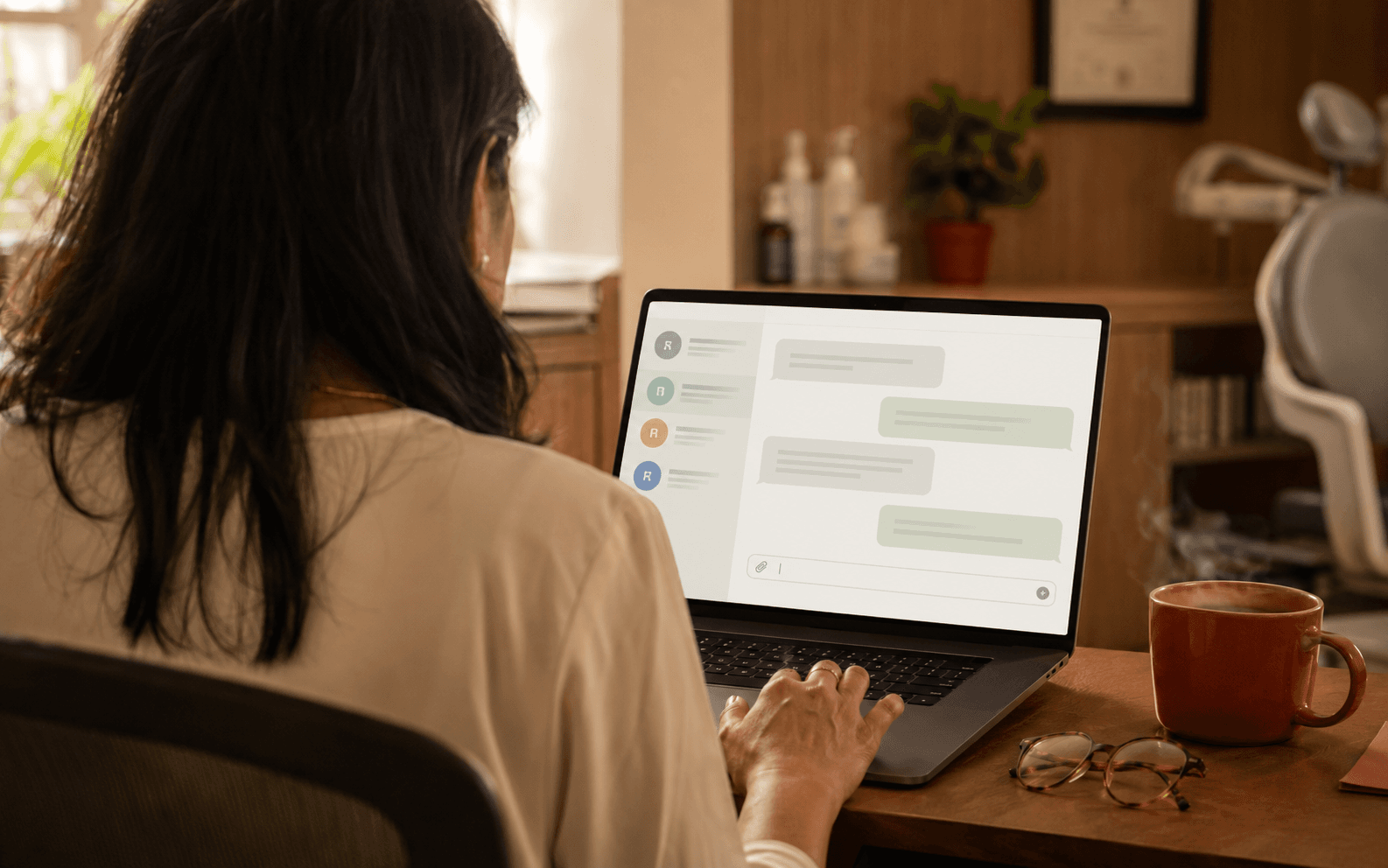 A dentist sits at her practice's front desk, four AI agent conversations open on her laptop, morning light from a window.